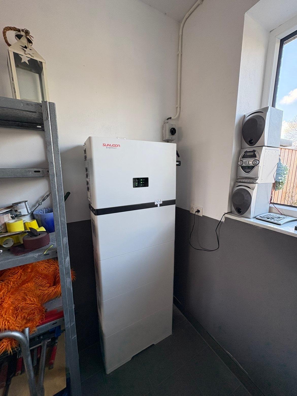 Door DES geplaatste witte batterij met zichtbare bekabeling langs de wand.