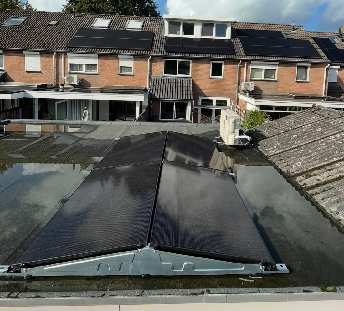 Zonnepanelen op een plat dak op de voorgrond, met zonnepanelen op de pannendaken van de woningen erachter.